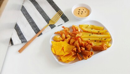 Minimalist food photography of mix platter served on a white plate. The dish features crispy fried shrimp, French fries, fried crackers, and corn chips, accompanied by dipping sauces.
