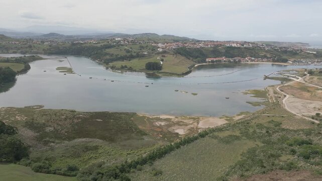 Drone footage with a backward flight over the Suances estuary, showing the Saja-Besaya river&rsquo;s deep channel bordered by stone breakwaters. A scenic meander of the estuary leads to the town of Suances