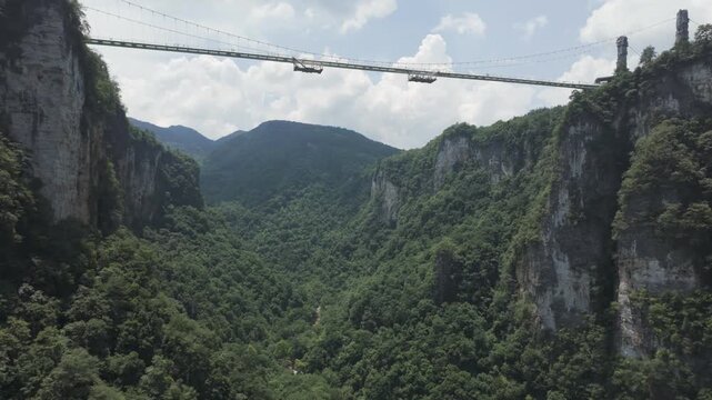 Breathtaking aerial view of the impressive Zhangjiajie Glass Bridge suspended high above a deep, verdant canyon, showcasing natural beauty and engineering.