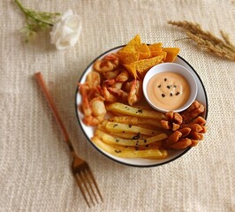 Minimalist food photography of mix platter served on a white plate. The dish features crispy fried shrimp, French fries, fried crackers, and corn chips, accompanied by dipping sauces.