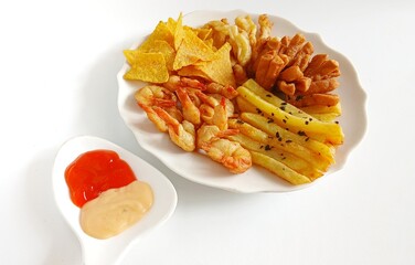 Minimalist food photography of mix platter served on a white plate. The dish features crispy fried shrimp, French fries, fried crackers, and corn chips, accompanied by dipping sauces.
