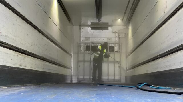 Worker using a high pressure washer to sanitize the front wall and cooling system of a cargo trailer interior