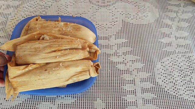 Close-up of a blue ceramic plate with several freshly made tamales in corn husks.