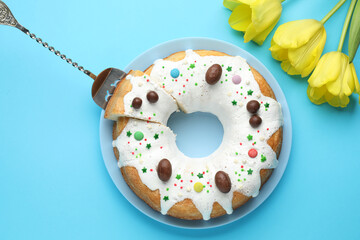 Naklejka premium Delicious Easter cake and yellow tulips on light blue background, flat lay