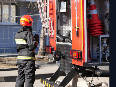 Fireman wearing protective gear and helmet using radio, standing beside a fire truck