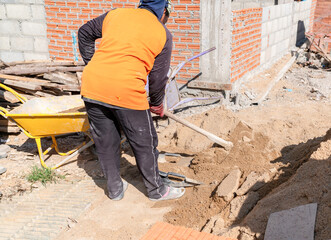Laborer preparing cement mix by shoveling sand at a residential construction project.