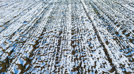 Fototapeta premium High angle aerial shot of a vast snowy field with repetitive lines of soil showing through in a winter environment