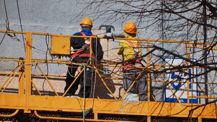 Construction workers applying stucco with safety harnesses on building facade