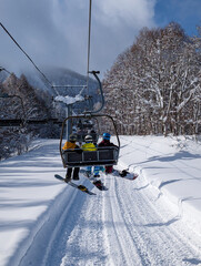 Back view of snowboarders ascending snowy slope on lift under blue winter sky