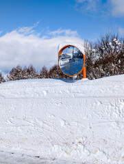 Orange traffic mirror rising above massive deep snow wall in Madarao, Japan