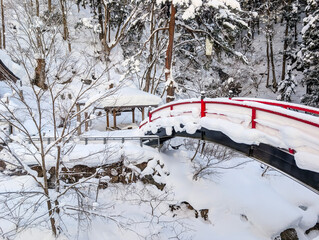 Traditional red arched bridge covered in heavy snow in Madarao forest, Japan