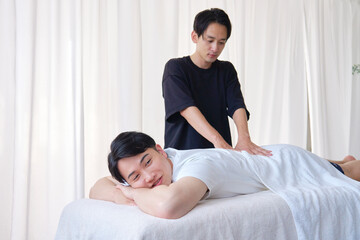 男性の腰をマッサージするマッサージ師