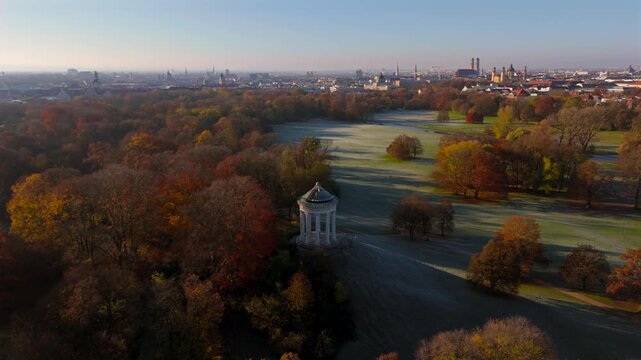 Luftaufnahme mit Drohne ueber den Englischen Garten in Muenchen am kalten Herbstmorgen. Sichtbar sind der Monopteros, frostige Wiesen sowie Frauenkirche, Theatinerkirche und Bayerische Staatskanzlei