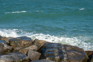 Peaceful sea waves crashing on rock and stone coast creating white foam splash in blue ocean water during summer nature landscape outdoor view