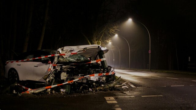 Severe car crash scene at night with police tape and heavy damage.