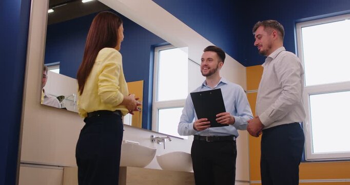 Happy couple with consultant salesman selects sink for home bathroom water needs in plumbing store, focusing on renovation in a professional setting with collaboration and support.