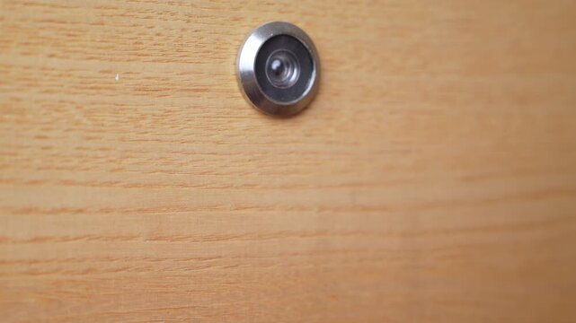 A small dog in a red suit reaches out to the peephole in a wooden door and knocks on the door.