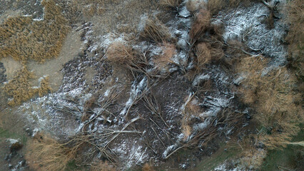 High altitude perspective of a wild frozen terrain with scattered dry grass and patches of snow displaying a unique winter texture of the earth surface from a drone view