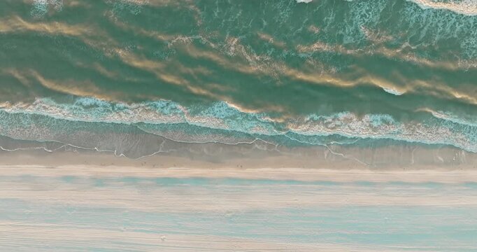Top down aerial view of ocean waves meeting sandy beach at sunset