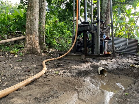 Rural water well drilling site with hose, pump equipment, and wet ground, capturing daily labor and water infrastructure development.