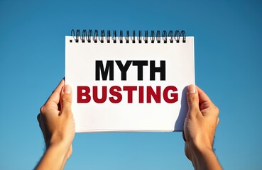 Fototapeta premium Hands hold notebook paper with MYTH BUSTING text against clear blue sky. Concept of challenging common beliefs, revealing truths, clarifying misconceptions with clear communication. Useful for