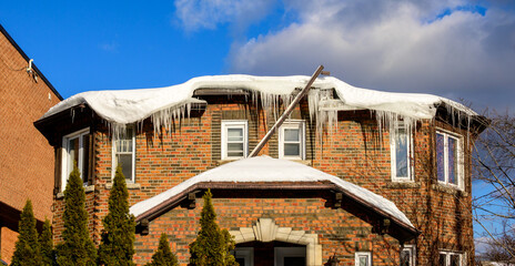 Ice dam buildup along the roof edge of an older brick apartment building, with snow accumulation and melting ice visible above upper-floor windows. © Michael Connor Photo