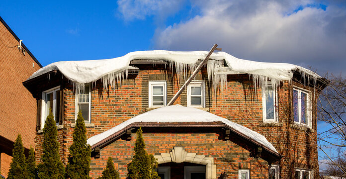 Ice dam buildup along the roof edge of an older brick apartment building, with snow accumulation and melting ice visible above upper-floor windows.