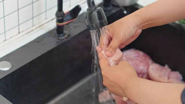 Close-up of hands cleaning fresh poultry meat in sink for meal preparation
