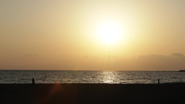 4K Wide shot of people walking along the beach at sunset in Chigasaki, Japan. Beautiful golden hour ocean scenery with silhouettes of people enjoying a stroll.