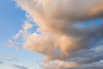 Obraz premium Gentle pastel-toned clouds float across a serene blue sky, illuminated by warm evening light and creating a peaceful, airy atmosphere.