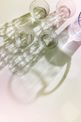 Transparent Water Glasses and water jug with shadows at sunlight on white, pastel color photo minimal style, aesthetic top view shiny cups sparkling at natural light, summer drink, composition