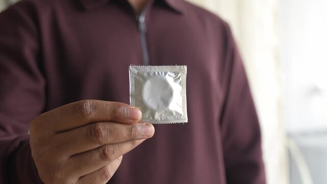 Showing packets of condoms held on finger.