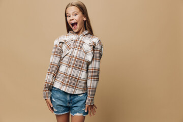 Girl with long hair wearing plaid shirt and denim shorts posing excitedly with open mouth and hands...