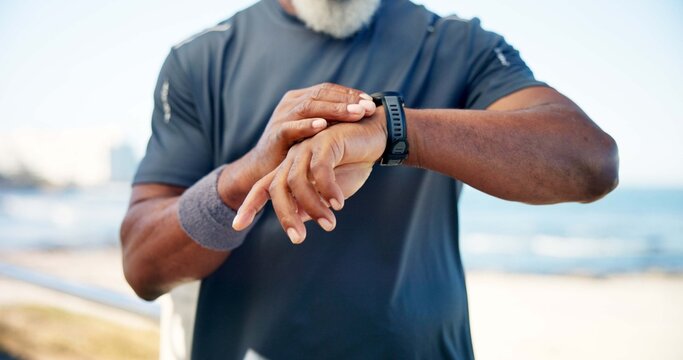 Old man, hands and smart watch by beach with fitness app, heart rate tracker and monitor performance. Senior person, runner and workout break by ocean with tech, check pace and wellness notification.