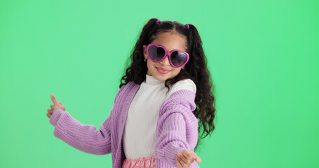 Naklejka premium Dance, kid and sunglasses on green screen with smile, space and casual fashion in studio. Child, shades and moving to music with rhythm, stylish accessory and cool girl with happiness on background