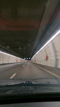 Stabilized vertical hyperlapse POV from inside a car driving through illuminated M30 bypass tunnel in Madrid, entering from A3 and emerging toward A6 highway urban traffic flow.