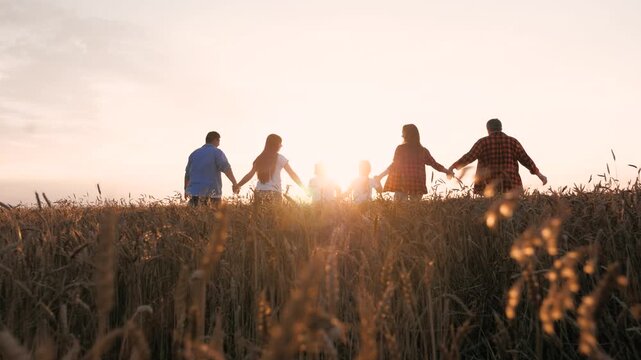 Happy family relatives running together at sunny sunset wheat field back view. Joyful man woman and kids relaxing together having fun enjoy freedom outdoor agriculture harvest meadow sky horizon