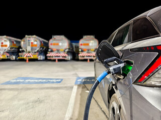 Fototapeta premium Electric car charging with fuel trucks in background