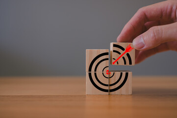 Hand picking wood block with darts target in Business goal and success concept. Initiation for planning to reach target. Darts target aim icon on wooden cubes on table grey background. Copy space