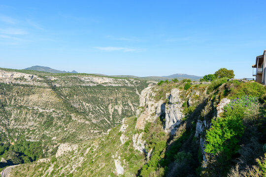 Steep limestone cliffs covered with green vegetation rise above a deep canyon under a clear blue sky at Cirque de Navacelles. The rugged landscape feels expansive and wild.