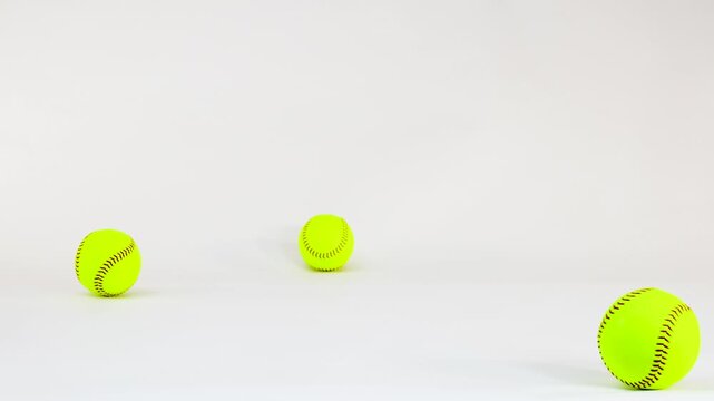 Optic Yellow Softballs Bouncing and Rolling Across a White Background