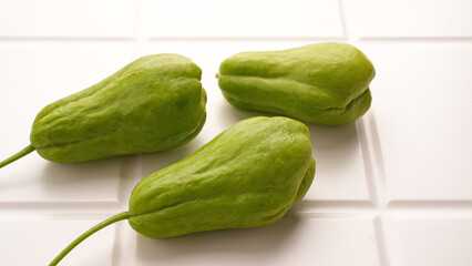 A pile of green chayote squash on white table