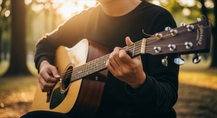 Obraz premium Man playing acoustic guitar outdoors during golden hour sunset, enjoying music