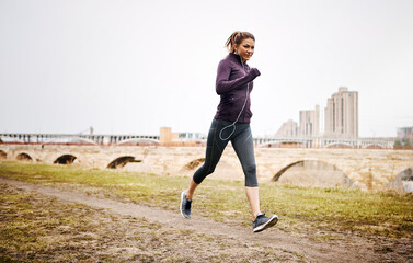 Fototapeta premium Earphones, running and woman in city for workout, exercise or marathon training outdoor with music. Audio tech, sports and female athlete listening to playlist or radio for cardio fitness in town.