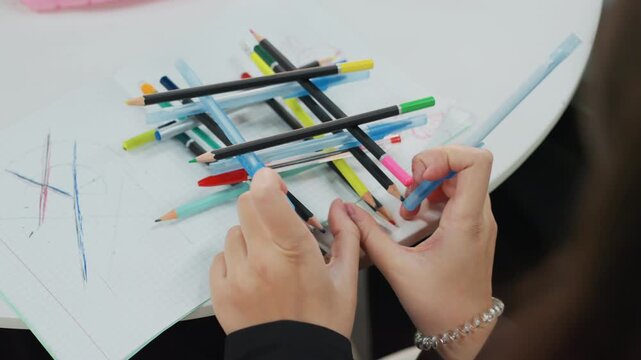 student arranging colored pencils on notebook, hands building tic tac toe grid with ruler and markers, closeup of desk with sketches and scattered stationery, calm focused study mood showcasing