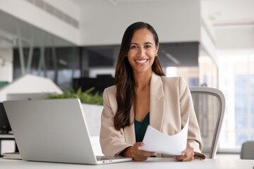 Portrait of happy female accountant or secretary sitting at desk with laptop, holding documents, making analysis, prepare agreement, review contract details, feel satisfied with productive workflow
