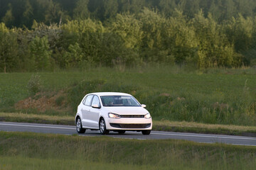 Fototapeta premium Urban hatchback driving through open green fields
