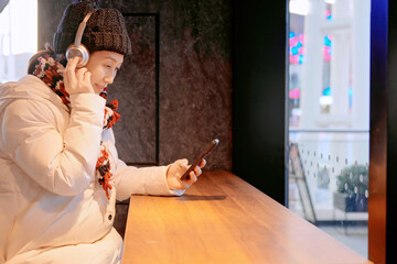 Woman in Winter Attire Using Smartphone with Headphones