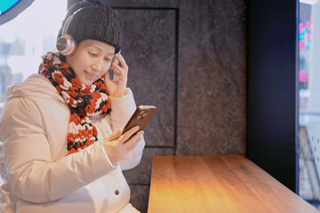 Woman in winter clothing using smartphone with headphones