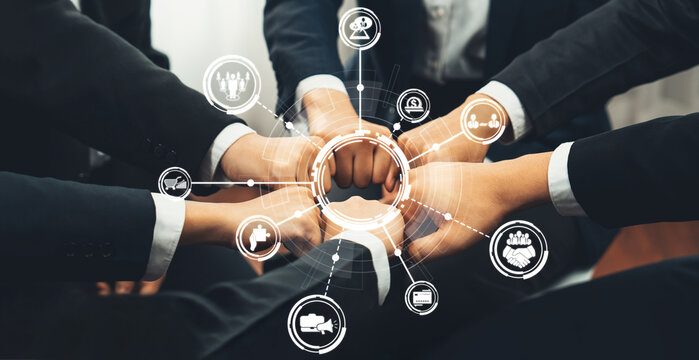 A group of diverse business professionals engages in a fist bump, symbolizing teamwork and collaboration, with digital icons enhancing the sense of connection and innovation. Amity
